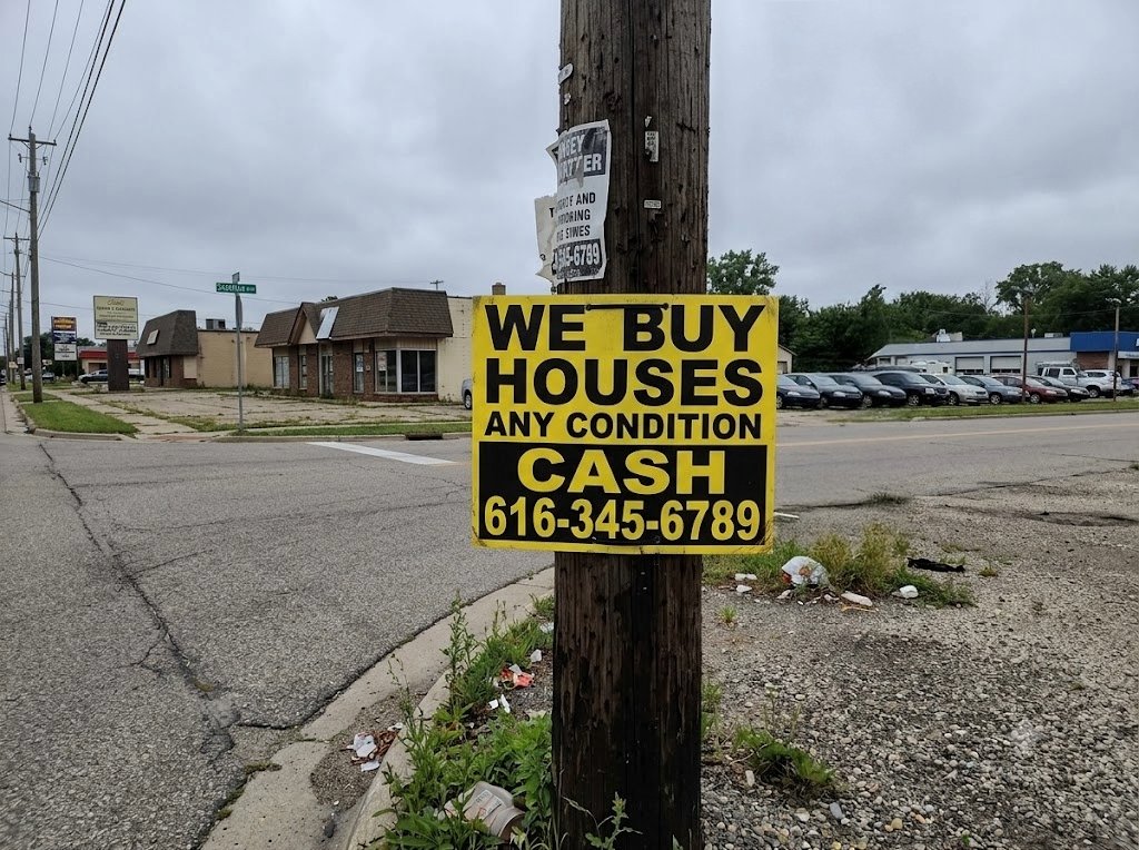A We Buy Houses for cash sign stapled to a utility pole at a West Michigan intersection